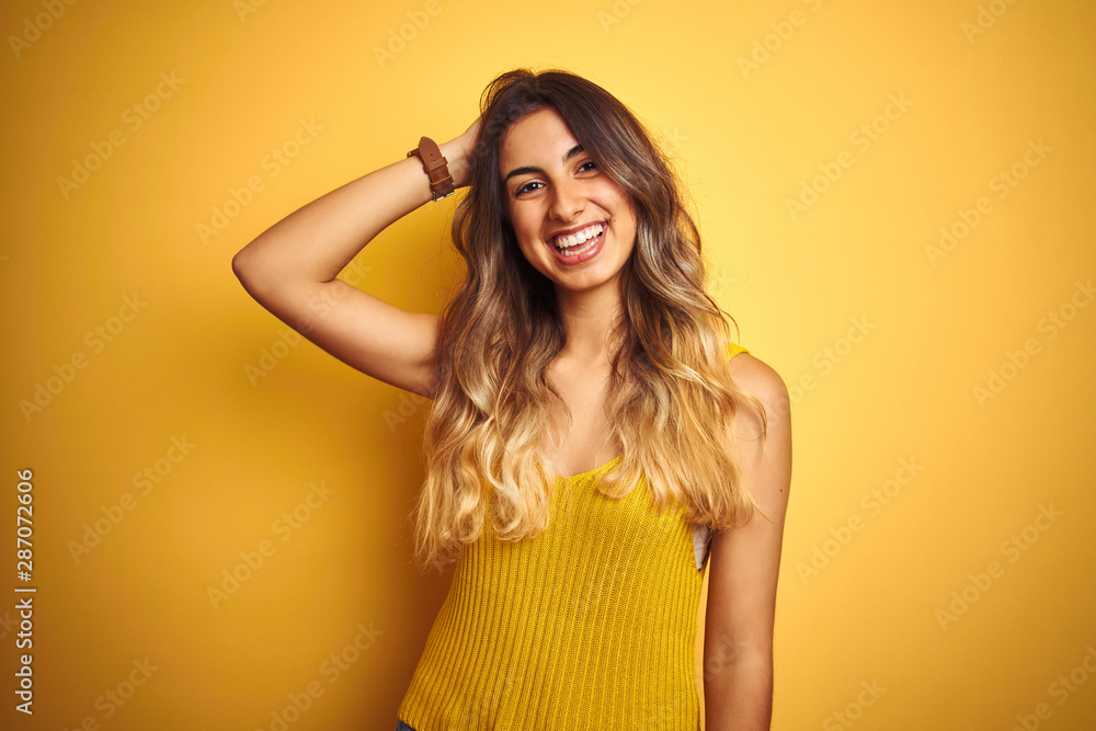 Young beautiful woman wearing t-shirt over yellow isolated background smiling confident touching hair with hand up gesture, posing attractive and fashionable Young beautiful woman wearing t-shirt over yellow isolated background smiling confident touching hair with hand up gesture, posing attractive and fashionable