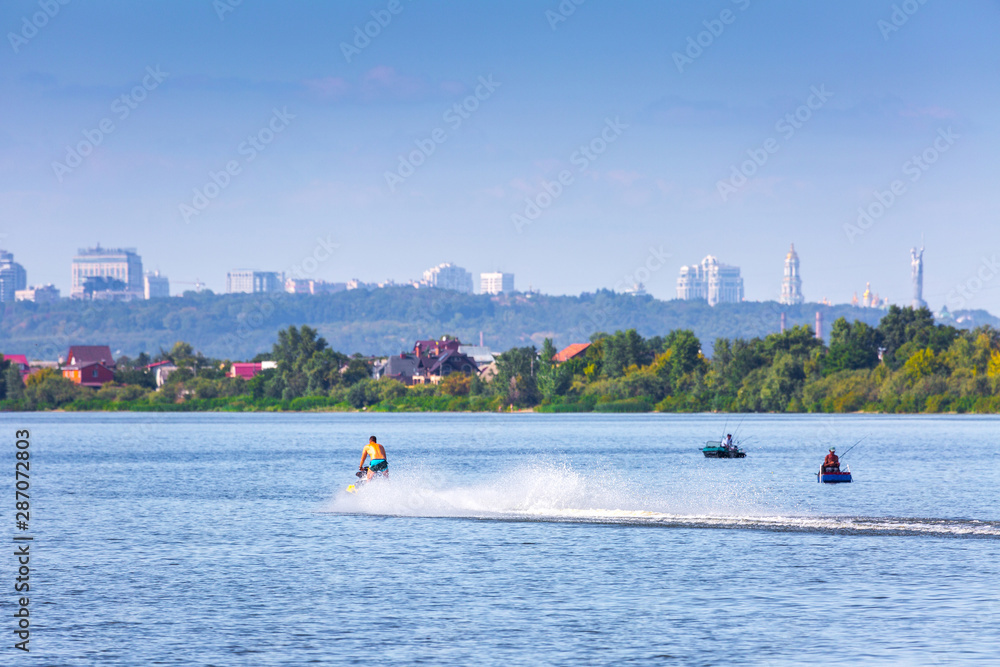 Obraz premium Summer sunny hot evening. Modern residential areas southern suburbs and midtown on hills in Kyiv on the right bank of the Dnipro River. Fishermen on boats on foreground. Kyiv. Ukraine. Aug. 28, 2019