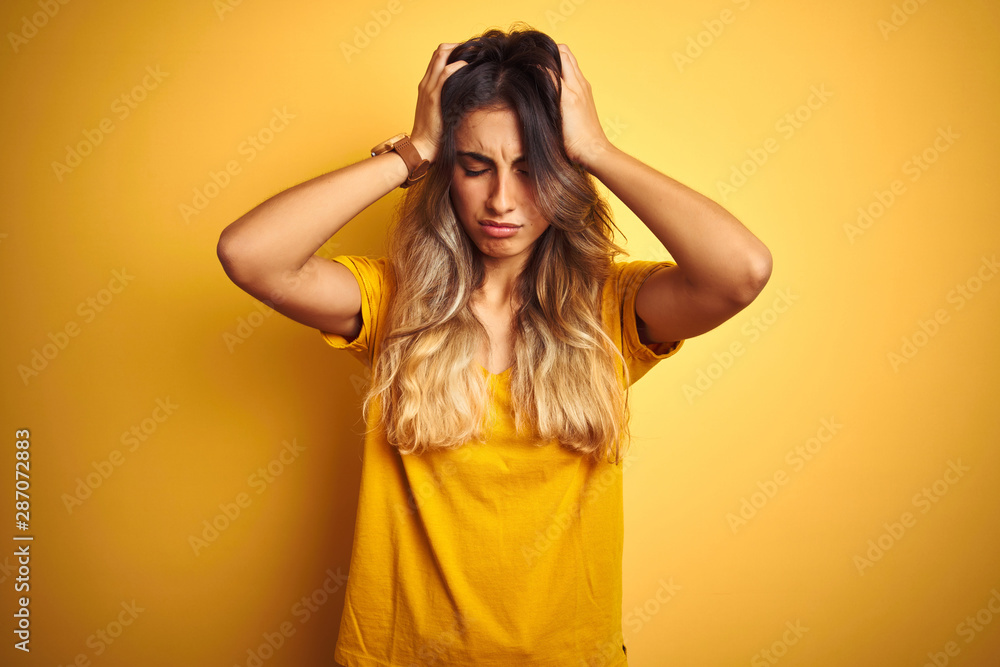 Young beautiful woman wearing t-shirt over yellow isolated background suffering from headache desperate and stressed because pain and migraine. Hands on head. Young beautiful woman wearing t-shirt over yellow isolated background suffering from headache desperate and stressed because pain and migraine. Hands on head.