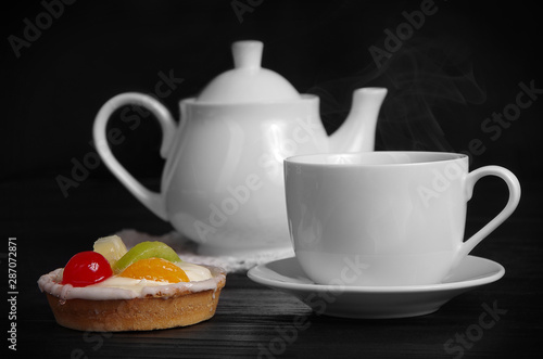 cup of hot tea with cake and teapot on the table