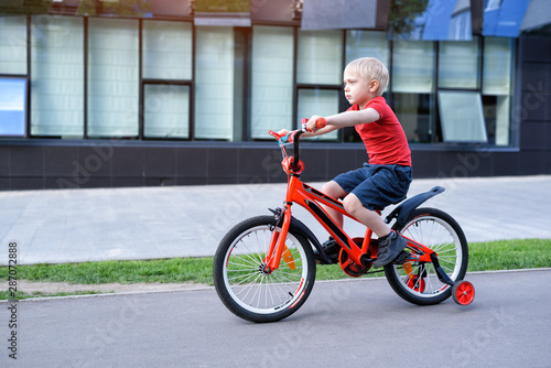 Fototapeta Naklejka Na Ścianę i Meble -  Handsome blond boy rides on a children's bicycle. Urban background