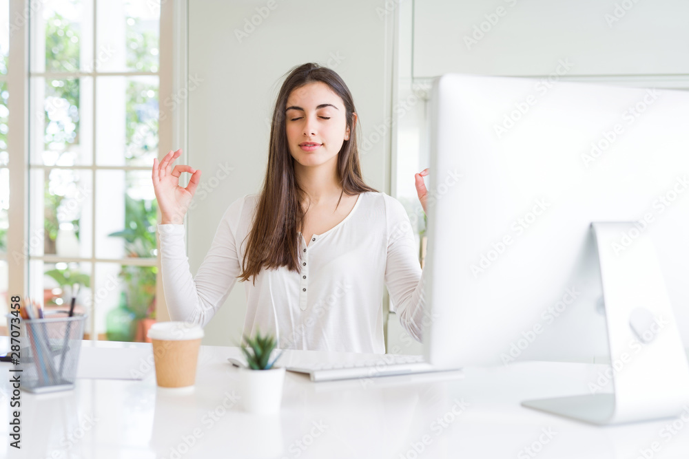 Beautiful young woman working using computer relax and smiling with eyes closed doing meditation gesture with fingers. Yoga concept. Beautiful young woman working using computer relax and smiling with eyes closed doing meditation gesture with fingers. Yoga concept.