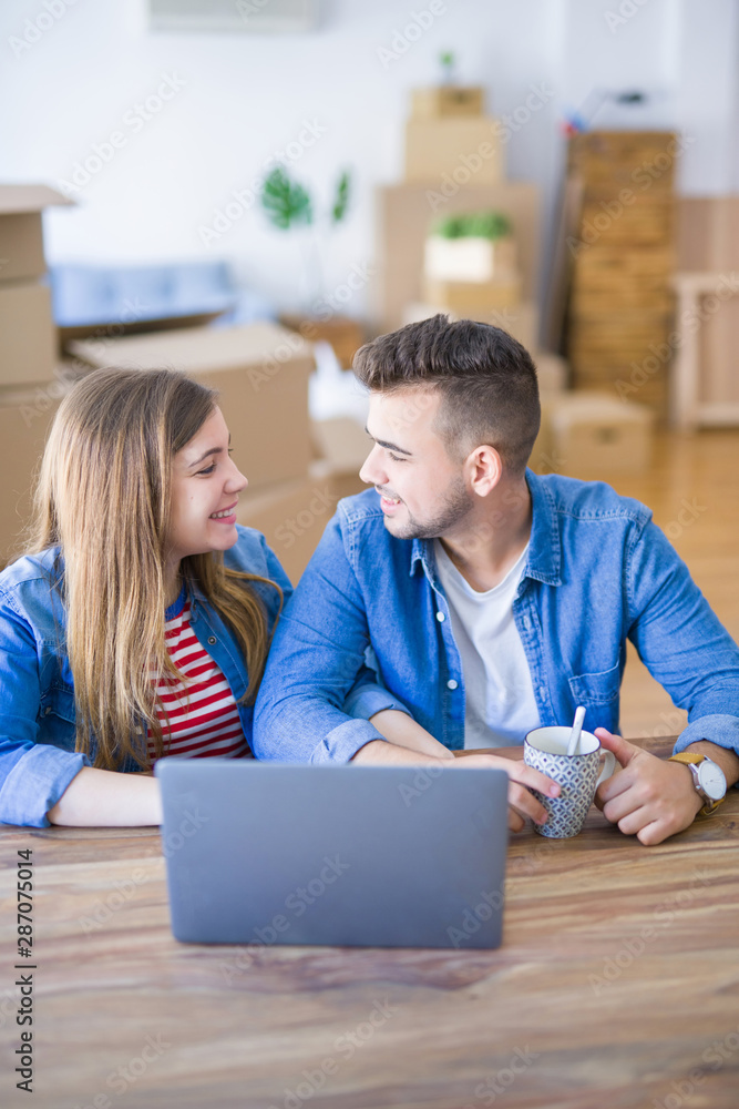 Young couple relaxing drinking a coffee and using the computer laptop around cardboard boxes, very happy moving to a new house Young couple relaxing drinking a coffee and using the computer laptop around cardboard boxes, very happy moving to a new house