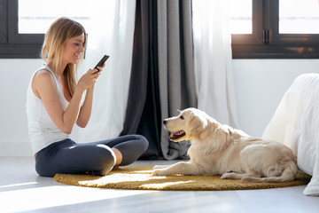 Pretty young woman taking photographs to her dog while staying on the floor at home.