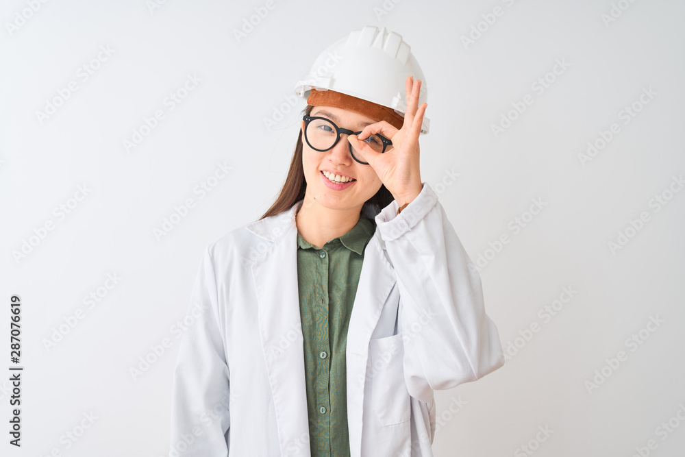 Young chinese engineer woman wearing coat helmet glasses over isolated white background doing ok gesture with hand smiling, eye looking through fingers with happy face. Young chinese engineer woman wearing coat helmet glasses over isolated white background doing ok gesture with hand smiling, eye looking through fingers with happy face.