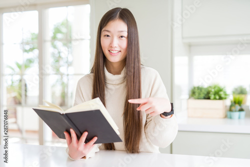 Beautiful Asian woman reading a book very happy pointing with hand and finger © Krakenimages.com