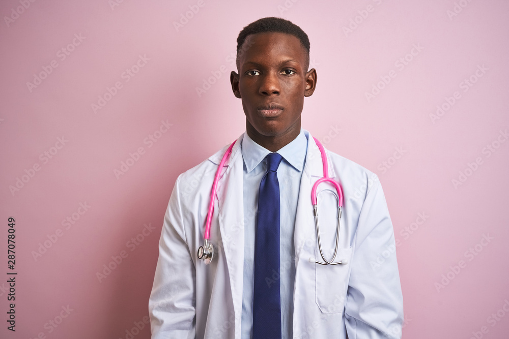 African american doctor man wearing stethoscope standing over isolated pink background with serious expression on face. Simple and natural looking at the camera. African american doctor man wearing stethoscope standing over isolated pink background with serious expression on face. Simple and natural looking at the camera.
