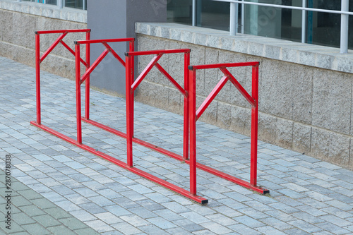 Red steel or iron parking place for bicycles standing on gray pavement by office or apartment building