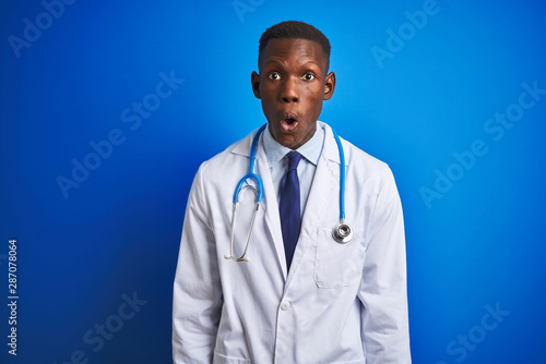 African american doctor man wearing stethoscope standing over isolated blue background afraid and shocked with surprise expression, fear and excited face.
