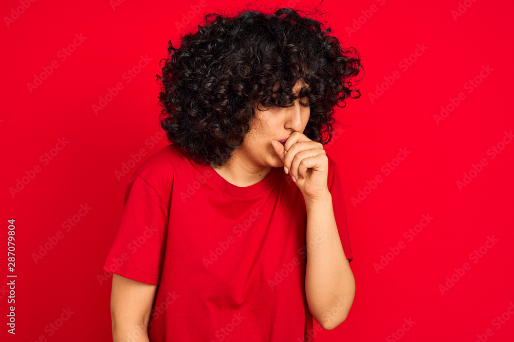 Young arab woman with curly hair wearing casual t-shirt over isolated red background feeling unwell and coughing as symptom for cold or bronchitis. Healthcare concept. Young arab woman with curly hair wearing casual t-shirt over isolated red background feeling unwell and coughing as symptom for cold or bronchitis. Healthcare concept.