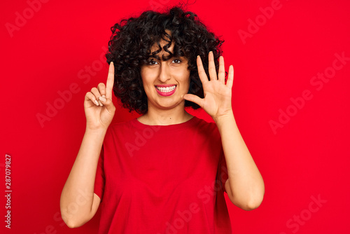 Young arab woman with curly hair wearing casual t-shirt over isolated red background showing and pointing up with fingers number six while smiling confident and happy.
