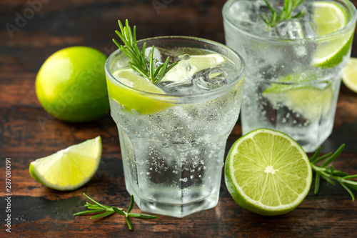 Gin and Tonic Alcohol drink with Lime, Rosemary and ice on wooden table