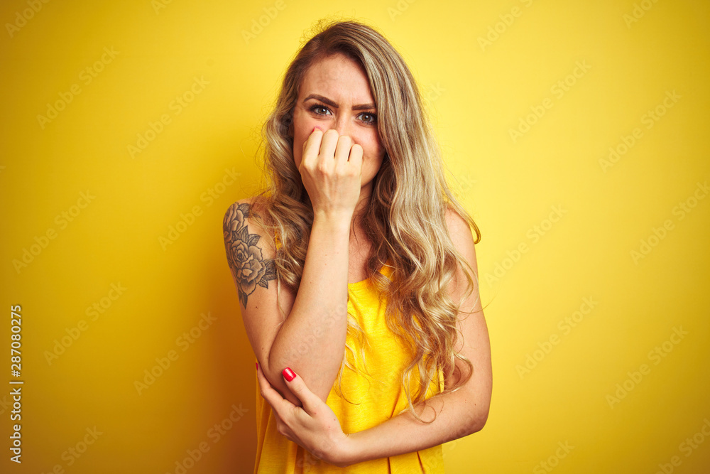 Ταπετσαρία Young beautiful woman wearing t-shirt standing over yellow isolated background looking stressed and nervous with hands on mouth biting nails