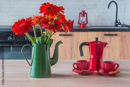 Breakfast in the kitchen. Red coffee pot and two cups of coffee, bouquet of red zinnia flowers in the green vintage coffee pot in the modern kitchen photo