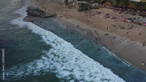 Aerial top view of sandy Dreamland beach, ocean and many tourists in water. Evening. Bali island, Indnesia photo