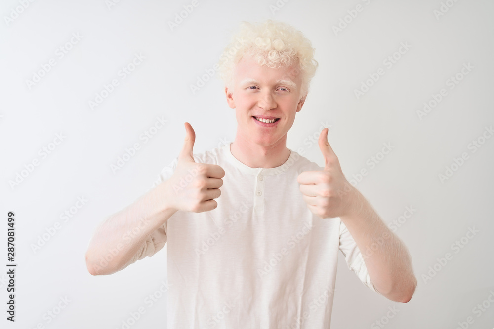Young albino blond man wearing casual t-shirt standing over isolated white background success sign doing positive gesture with hand, thumbs up smiling and happy. Cheerful expression