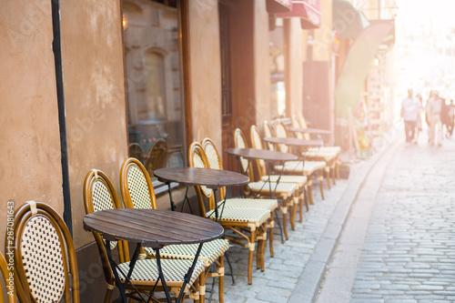 Fototapeta Naklejka Na Ścianę i Meble -  Empty tables in between dining hours. Old fashioned cafe terrace in a summer day