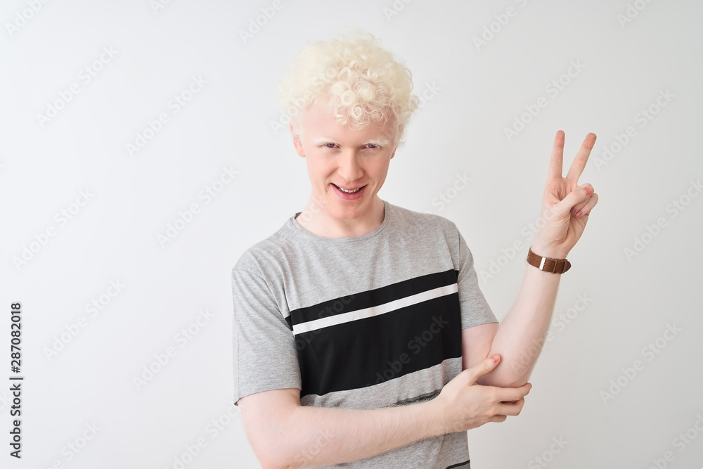 Young albino blond man wearing casual t-shirt standing over isolated white background smiling with happy face winking at the camera doing victory sign. Number two. Young albino blond man wearing casual t-shirt standing over isolated white background smiling with happy face winking at the camera doing victory sign. Number two.