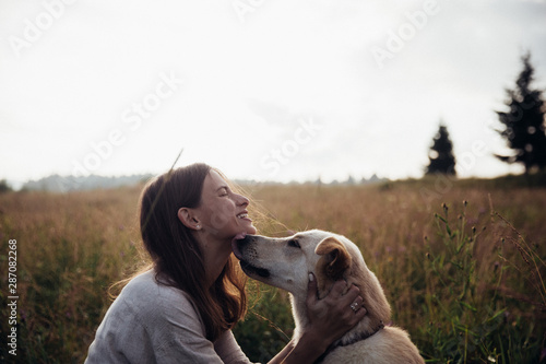 Beautiful young woman relaxed and carefree enjoying a summer sunset with her lovely dog on the straw field background