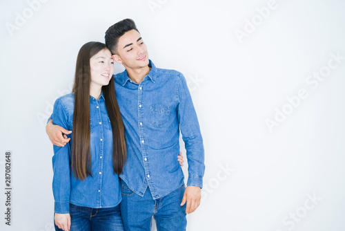Beautiful young asian couple over white isolated background looking away to side with smile on face, natural expression. Laughing confident.