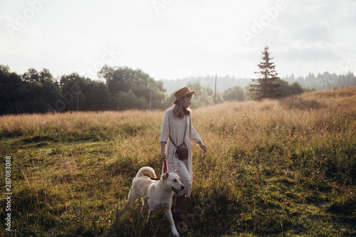 Beautiful young woman relaxed and carefree enjoying a summer sunset with her lovely dog on the straw field background