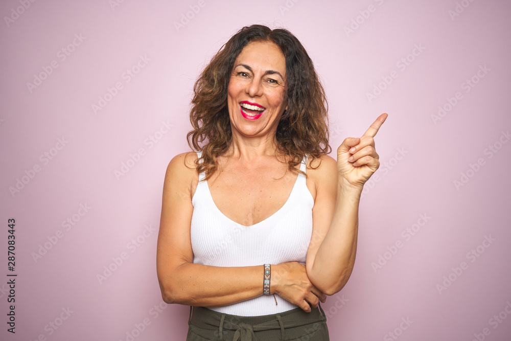 Middle age senior woman standing over pink isolated background with a big smile on face, pointing with hand and finger to the side looking at the camera. Middle age senior woman standing over pink isolated background with a big smile on face, pointing with hand and finger to the side looking at the camera.