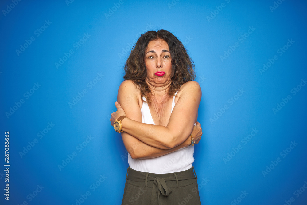 Middle age senior woman with curly hair standing over blue isolated background shaking and freezing for winter cold with sad and shock expression on face Middle age senior woman with curly hair standing over blue isolated background shaking and freezing for winter cold with sad and shock expression on face
