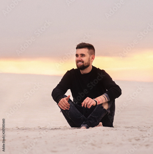 Beautiful young mansitting barefoot on sand in desert enjoying nature and the sun. photo