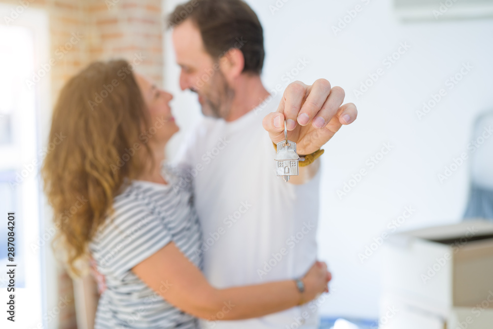 Middle age senior romantic couple holding and showing house keys, hugging and smiling happy for moving to a new home Middle age senior romantic couple holding and showing house keys, hugging and smiling happy for moving to a new home