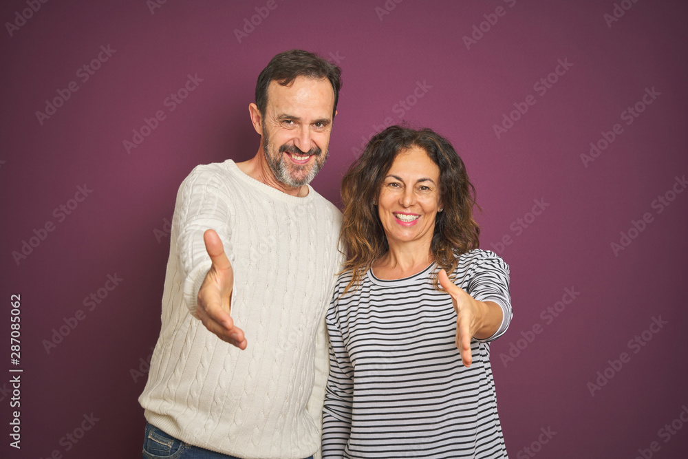 Obraz premium Beautiful middle age couple wearing winter sweater over isolated purple background smiling friendly offering handshake as greeting and welcoming. Successful business.