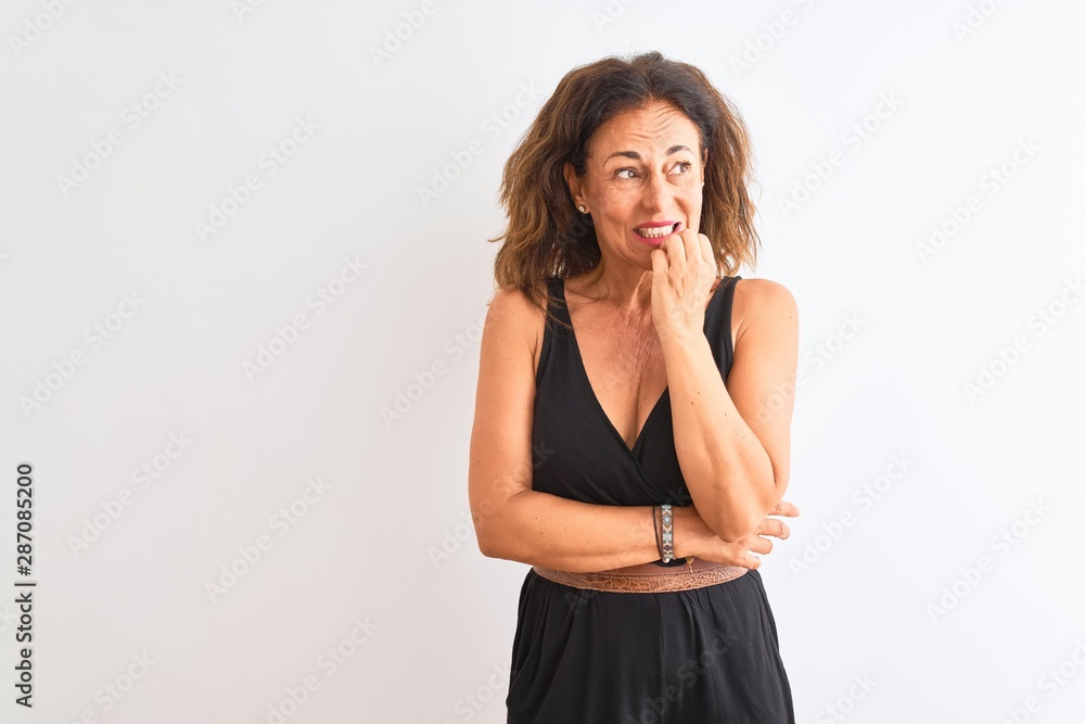 Middle age woman wearing black casual dress standing over isolated white background looking stressed and nervous with hands on mouth biting nails. Anxiety problem. Middle age woman wearing black casual dress standing over isolated white background looking stressed and nervous with hands on mouth biting nails. Anxiety problem.