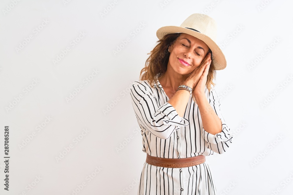Middle age businesswoman wearing striped dress and hat over isolated white background sleeping tired dreaming and posing with hands together while smiling with closed eyes. Middle age businesswoman wearing striped dress and hat over isolated white background sleeping tired dreaming and posing with hands together while smiling with closed eyes.