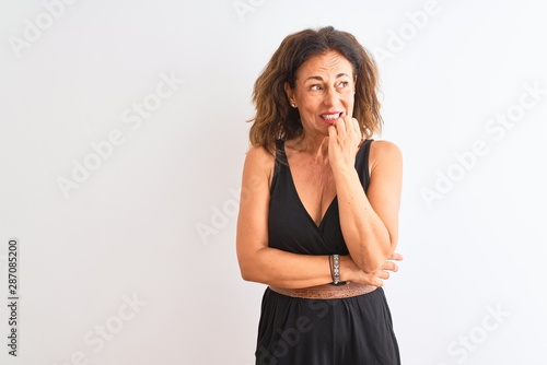 Middle age woman wearing black casual dress standing over isolated white background looking stressed and nervous with hands on mouth biting nails. Anxiety problem. © Krakenimages.com