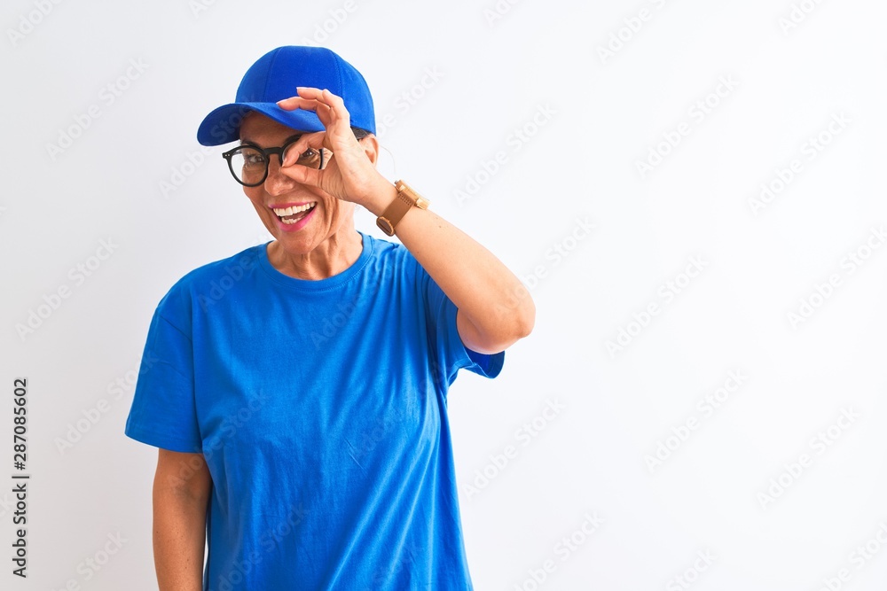 Senior deliverywoman wearing cap and glasses standing over isolated white background doing ok gesture with hand smiling, eye looking through fingers with happy face.