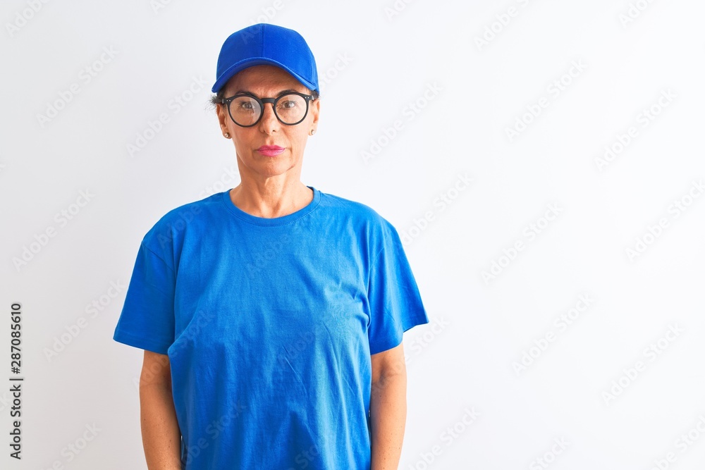 Senior deliverywoman wearing cap and glasses standing over isolated white background with serious expression on face. Simple and natural looking at the camera.