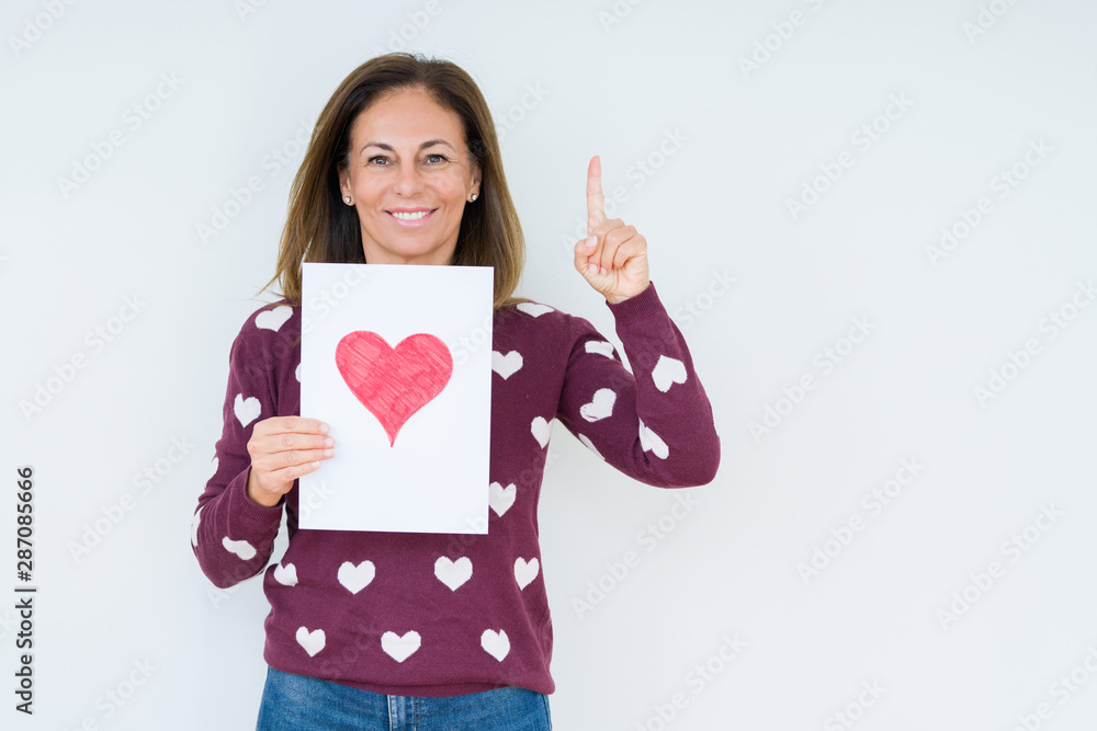 Middle age woman holding card gift with red heart over isolated background surprised with an idea or question pointing finger with happy face, number one