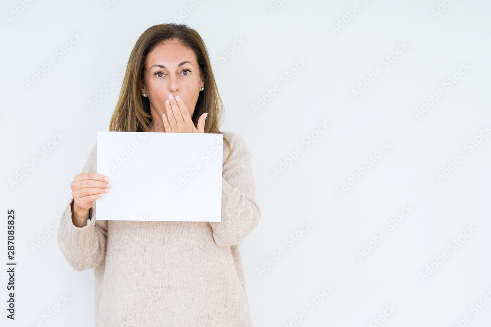 Middle age woman holding blank paper sheet over isolated background cover mouth with hand shocked with shame for mistake, expression of fear, scared in silence, secret concept Middle age woman holding blank paper sheet over isolated background cover mouth with hand shocked with shame for mistake, expression of fear, scared in silence, secret concept