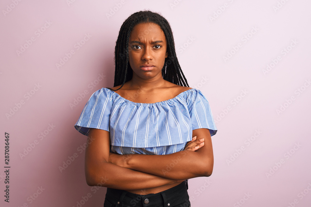 Obraz premium African american woman wearing striped t-shirt standing over isolated pink background skeptic and nervous, disapproving expression on face with crossed arms. Negative person.