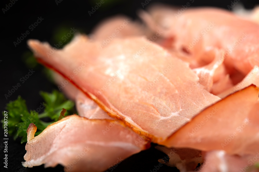 Thin sliced smoked pork ham on a dark slate with herbs Thin sliced smoked pork ham on a dark slate with herbs