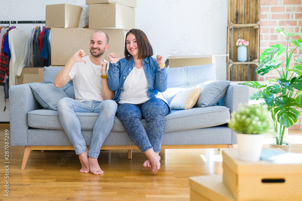 Young couple sitting on the sofa arround cardboard boxes moving to a new house looking confident with smile on face, pointing oneself with fingers proud and happy. Young couple sitting on the sofa arround cardboard boxes moving to a new house looking confident with smile on face, pointing oneself with fingers proud and happy.