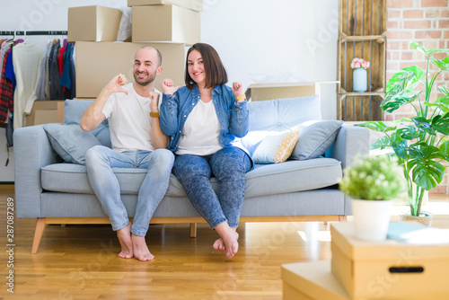 Young couple sitting on the sofa arround cardboard boxes moving to a new house looking confident with smile on face, pointing oneself with fingers proud and happy.