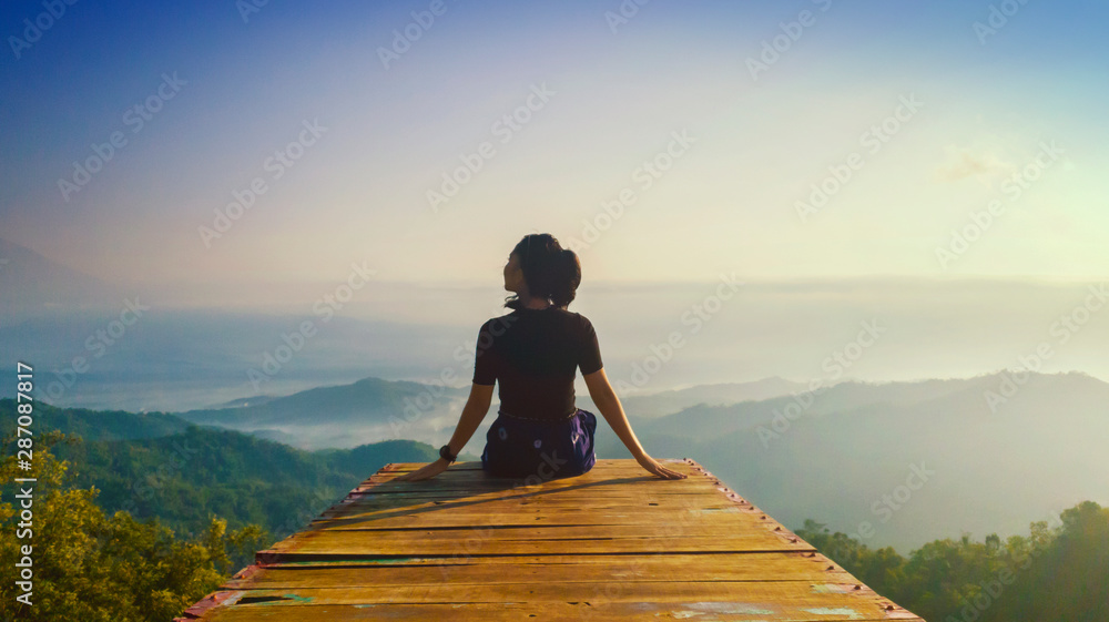 Young woman sits and enjoys Ngisis hill view - obrazy, fototapety, plakaty 