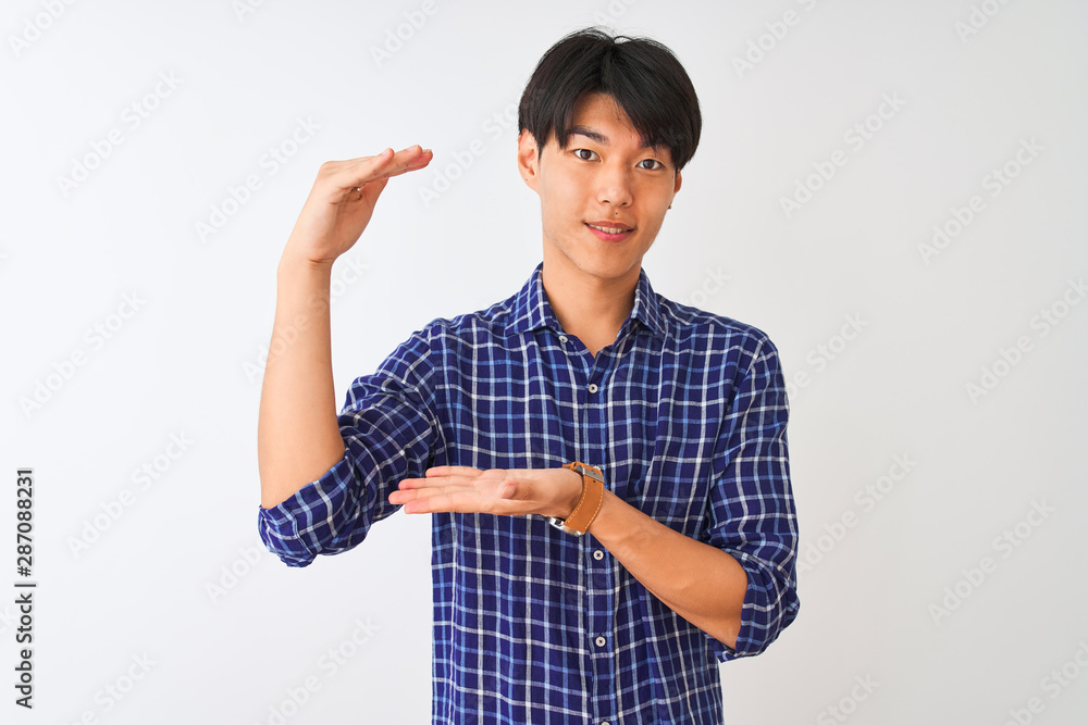 Young chinese man wearing casual blue shirt standing over isolated white background gesturing with hands showing big and large size sign, measure symbol. Smiling looking at the camera. Young chinese man wearing casual blue shirt standing over isolated white background gesturing with hands showing big and large size sign, measure symbol. Smiling looking at the camera.