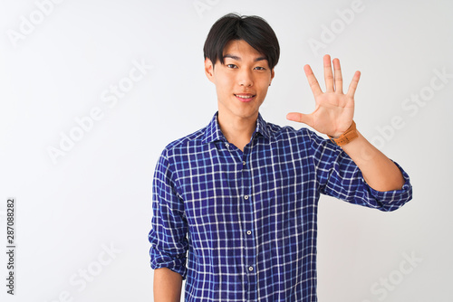 Young chinese man wearing casual blue shirt standing over isolated white background showing and pointing up with fingers number five while smiling confident and happy.