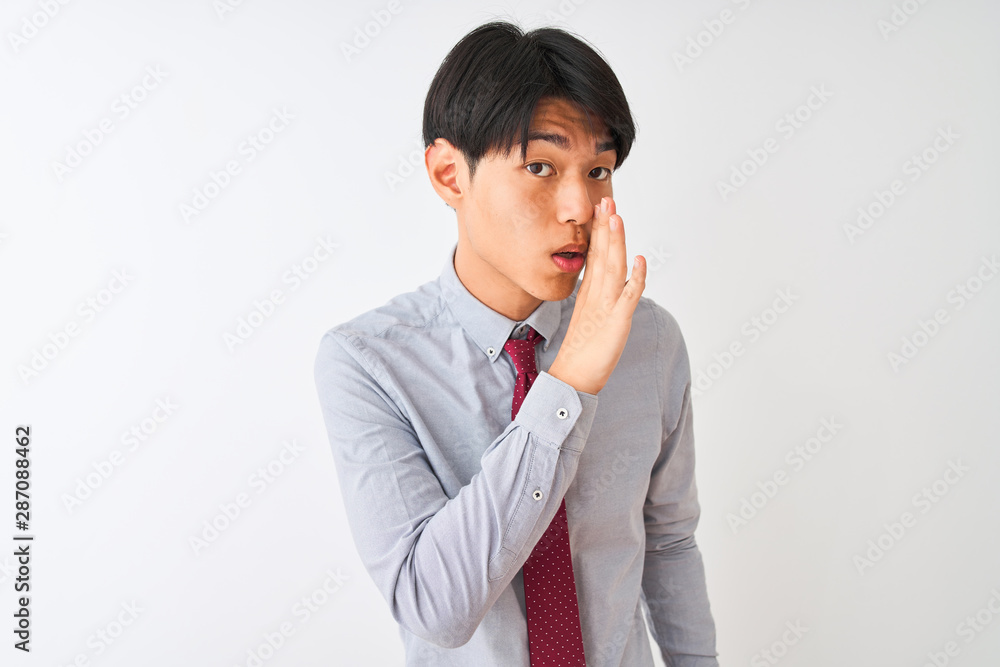 Chinese businessman wearing elegant tie standing over isolated white background hand on mouth telling secret rumor, whispering malicious talk conversation Chinese businessman wearing elegant tie standing over isolated white background hand on mouth telling secret rumor, whispering malicious talk conversation