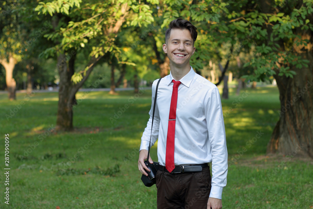 Stylishly dressed young man posing in a park. A SLR film camera hangs on his shoulder. Stylishly dressed young man posing in a park. A SLR film camera hangs on his shoulder.