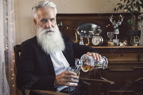 Fotografie Handsome bearded senior man pouring whiskey into the glass