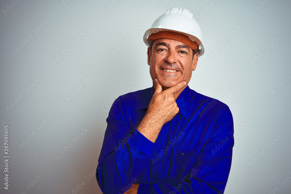 Handsome middle age worker man wearing uniform and helmet over isolated white background looking confident at the camera smiling with crossed arms and hand raised on chin. Thinking positive. Handsome middle age worker man wearing uniform and helmet over isolated white background looking confident at the camera smiling with crossed arms and hand raised on chin. Thinking positive.