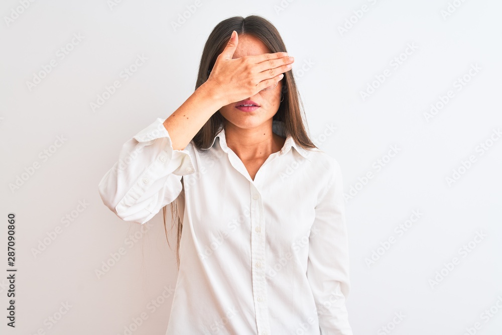 Young beautiful businesswoman wearing glasses standing over isolated white background covering eyes with hand, looking serious and sad. Sightless, hiding and rejection concept Young beautiful businesswoman wearing glasses standing over isolated white background covering eyes with hand, looking serious and sad. Sightless, hiding and rejection concept