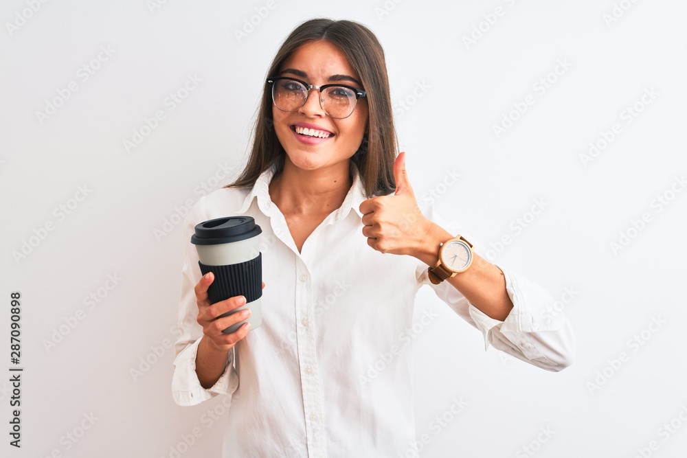 Young businesswoman wearing glasses drinking coffee over isolated white background happy with big smile doing ok sign, thumb up with fingers, excellent sign